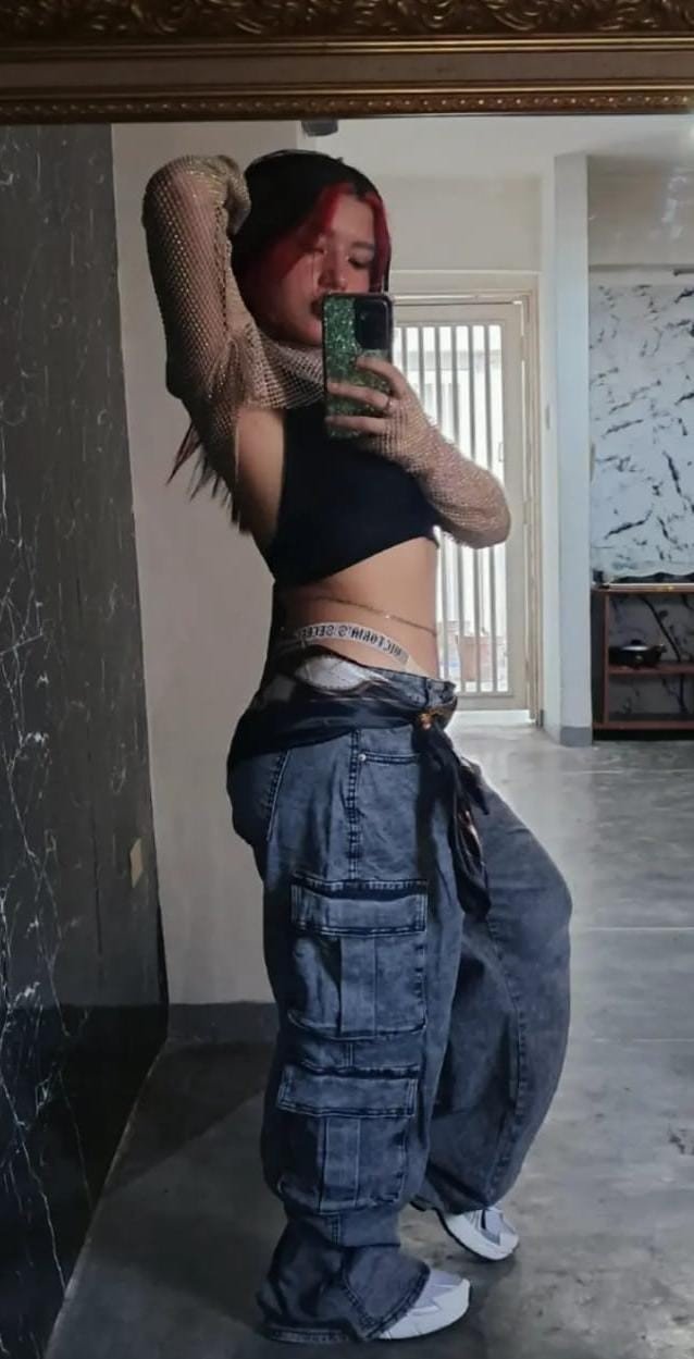 AYDI en una fotografía de espejo con vestuario urbano y cabello oscuro con detalles rojos.